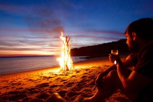 man sitting by a fire on the beach