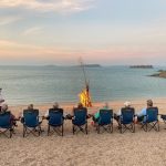 Guests enjoying the evening sunset whilst relaxing with a driftwood bonfire on a secluded beach