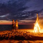 two people by a fire on a beach